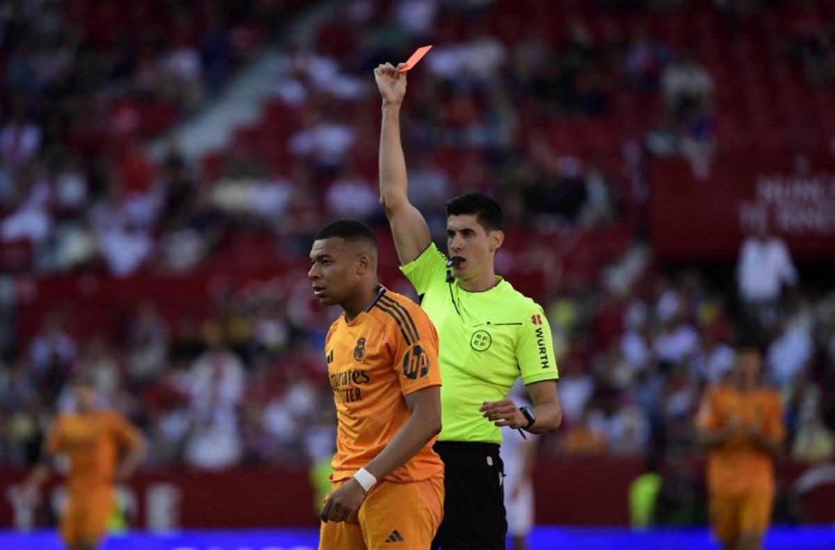 Real Madrid's French forward #09 Kylian Mbappe passes by Spanish referee Busquets Ferrer whot presents a red card to Sevilla's French defender #22 Loic Bade (OUT OF FRAME) during the Spanish league football match between Sevilla FC and Real Madrid CF at Ramon Sanchez Pizjuan Stadium in Seville on May 18, 2025.  CRISTINA QUICLER / AFP