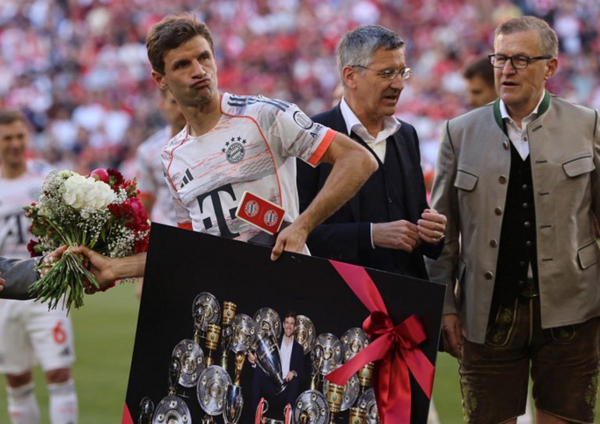 Bayern Munich's German forward #25 Thomas Mueller (L) walks away with a flower bouquet and a picture showing Muller inmid trophies ahead the German first division Bundesliga football match between Bayern Munich and Borussia Moenchengladbach in Munich on May 10, 2025.  Alexandra BEIER / AFP