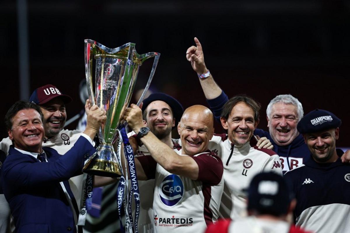 Bordeaux-Begles' owner Laurent Marti (L) and Bordeaux-Begles' French head coach Yannick Bru (C) celebrate with the trophy after winning the Champions Cup Final rugby union match between Northampton Saints and Bordeaux-Begles at the Principality Stadium in Cardiff, south Wales, on May 24, 2025. Bordeaux-Begles wins 28 - 20 against Northampton Saints. Anne-Christine POUJOULAT / AFP