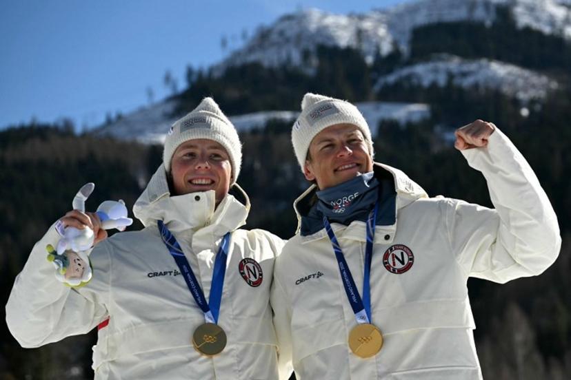 Gold medallists Norway's Johannes Hoesflot Klaebo (R) and Norway's Einar Hedegart celebrate on the podium for the men's team cross country free sprint final event of the Milano Cortina 2026 Winter Olympic Games at Tesero Cross-Country Skiing Stadium in Lago di Tesero (Val di Fiemme), on February 18, 2026.  Javier SORIANO / AFP