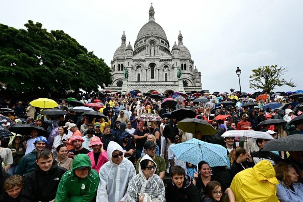 Spectators await the pack of riders (peloton) in the rain, at the foot the Sacre-Coeur Basilica on the Butte de Montmartre during the 21st and final stage of the 112th edition of the Tour de France cycling race, 132.3 km between Mantes-la-Ville and Paris' Champs-Elysees Avenue, on July 27, 2025.  Loic VENANCE / AFP