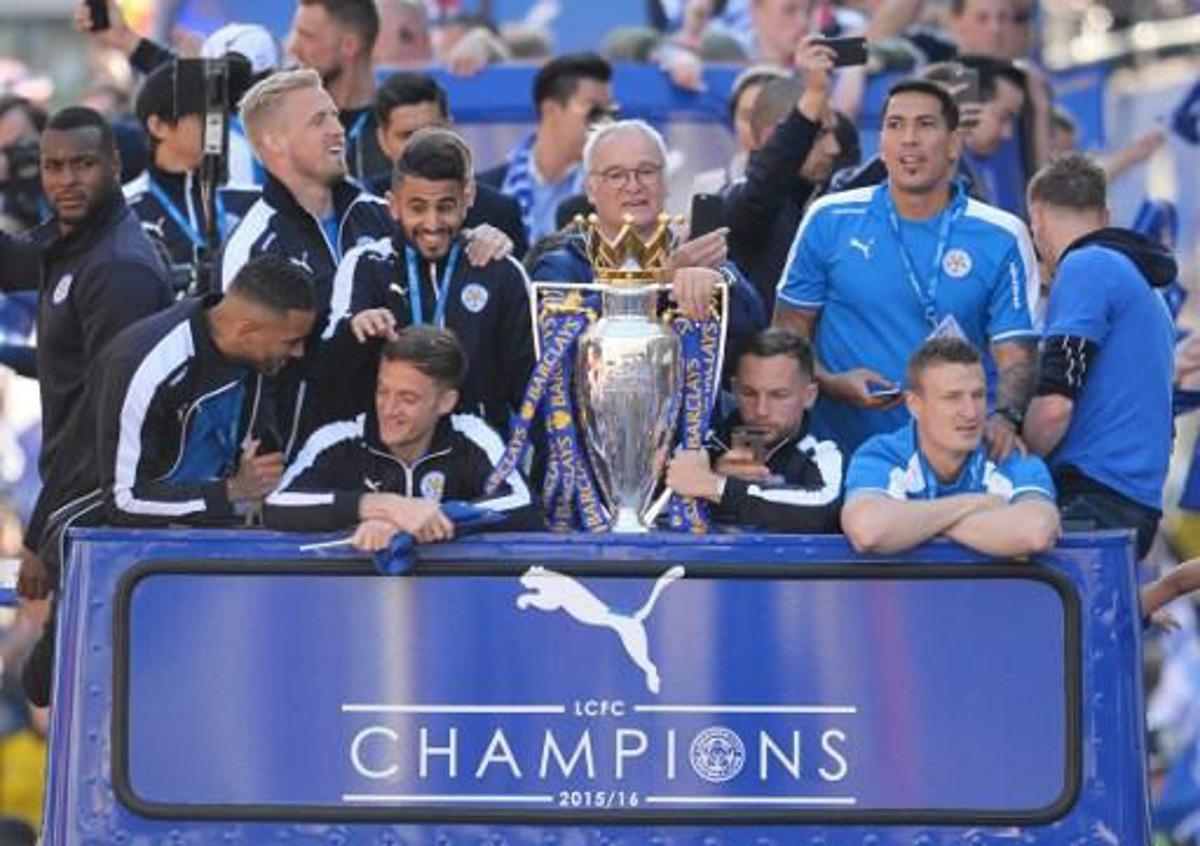 (L-R) Leicester City's English defender Wes Morgan, Leicester City's Danish goalkeeper Kasper Schmeichel, Leicester City's Algerian midfielder Riyad Mahrez, Leicester City's Italian manager Claudio Ranieri, Leicester City's English midfielder Danny Drinkwater, Leicester City's Argentinian striker Leonardo Ulloa and Leicester City's German defender Robert Huth stand with the Premier league trophy as the Leicester City team take part in an open-top bus parade through Leicester to celebrate winning the Premier League title on May 16, 2016.   / AFP PHOTO / GLYN KIRK