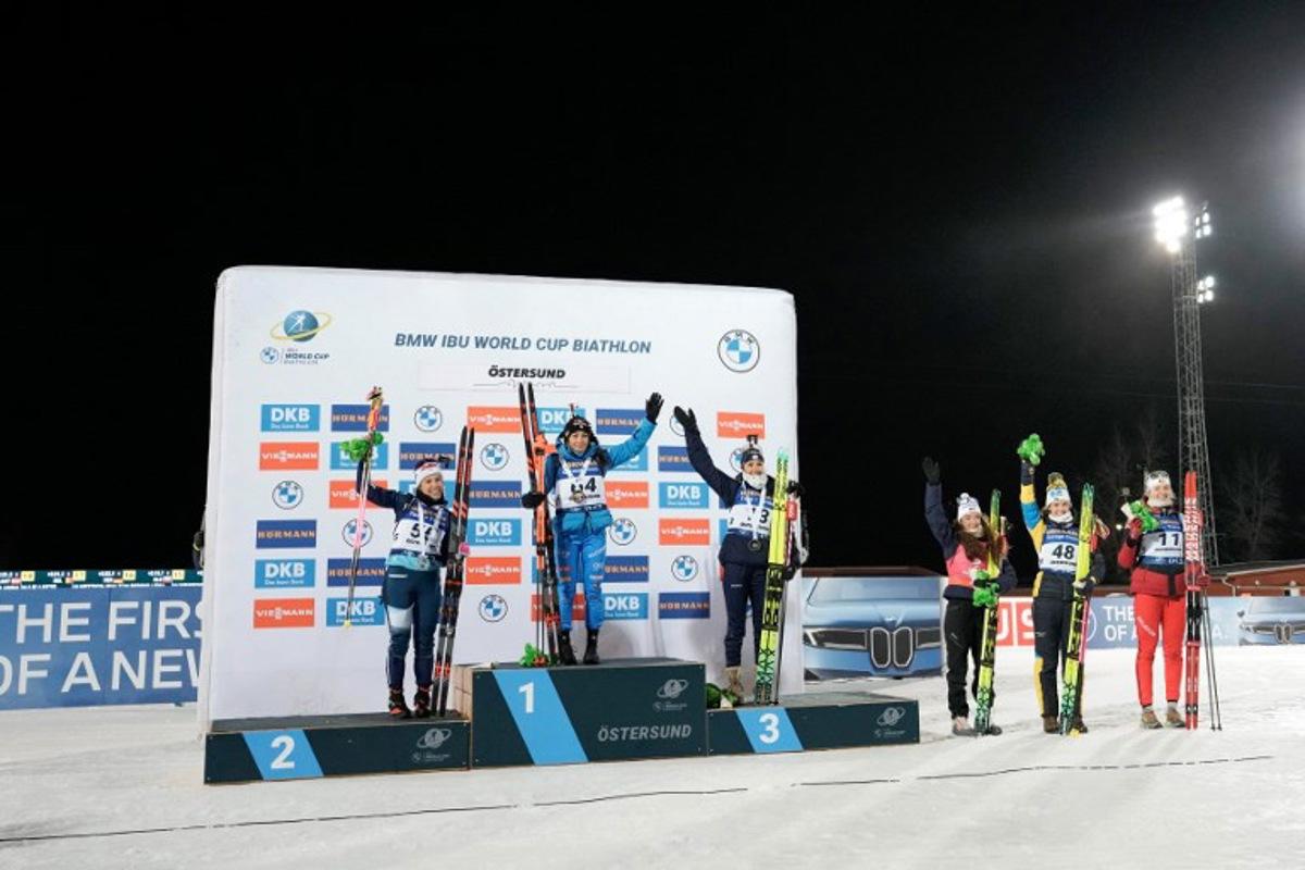 (L-R) Second placed Finland's Sonja Leinamo, first placed Italy's Dorothea Wierer and third placed France's Camille Bened celebrate on the podium after winning the women's 15km individual event of the IBU Biathlon World Cup in Oestersund, Sweden on December 2, 2025, followed next to the podium by fourth placed France's Lou Jeanmonnot, fifth placed Sweden's Hanna Oeberg and sixth placed Belgium's Maya Cloetens.  Bjorn LARSSON ROSVALL / TT NEWS AGENCY / AFP