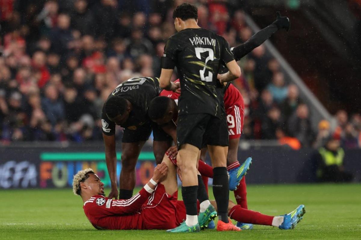Players care for Liverpool's French striker #22 Hugo Ekitike who lies injured during the UEFA Champions League quarter final, second-leg football match between Liverpool and Paris Saint-Germain at Anfield in Liverpool, north west England on April 14, 2026.  FRANCK FIFE / AFP