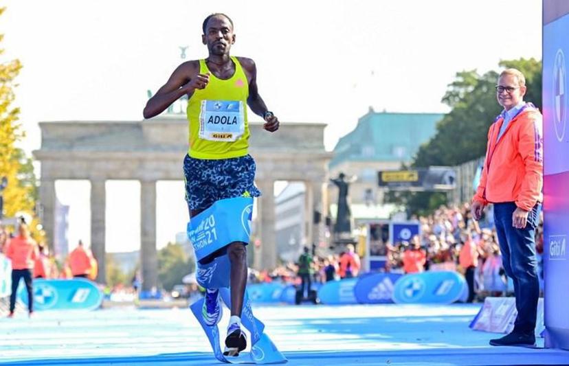 Ethiopia's GuyeAdola runs to win the Berlin Marathon on September 26, 2021 in front of Brandenburg Gate in Berlin, as Berlin's Mayor Michael Mueller (R) looks on.   Tobias SCHWARZ / AFP