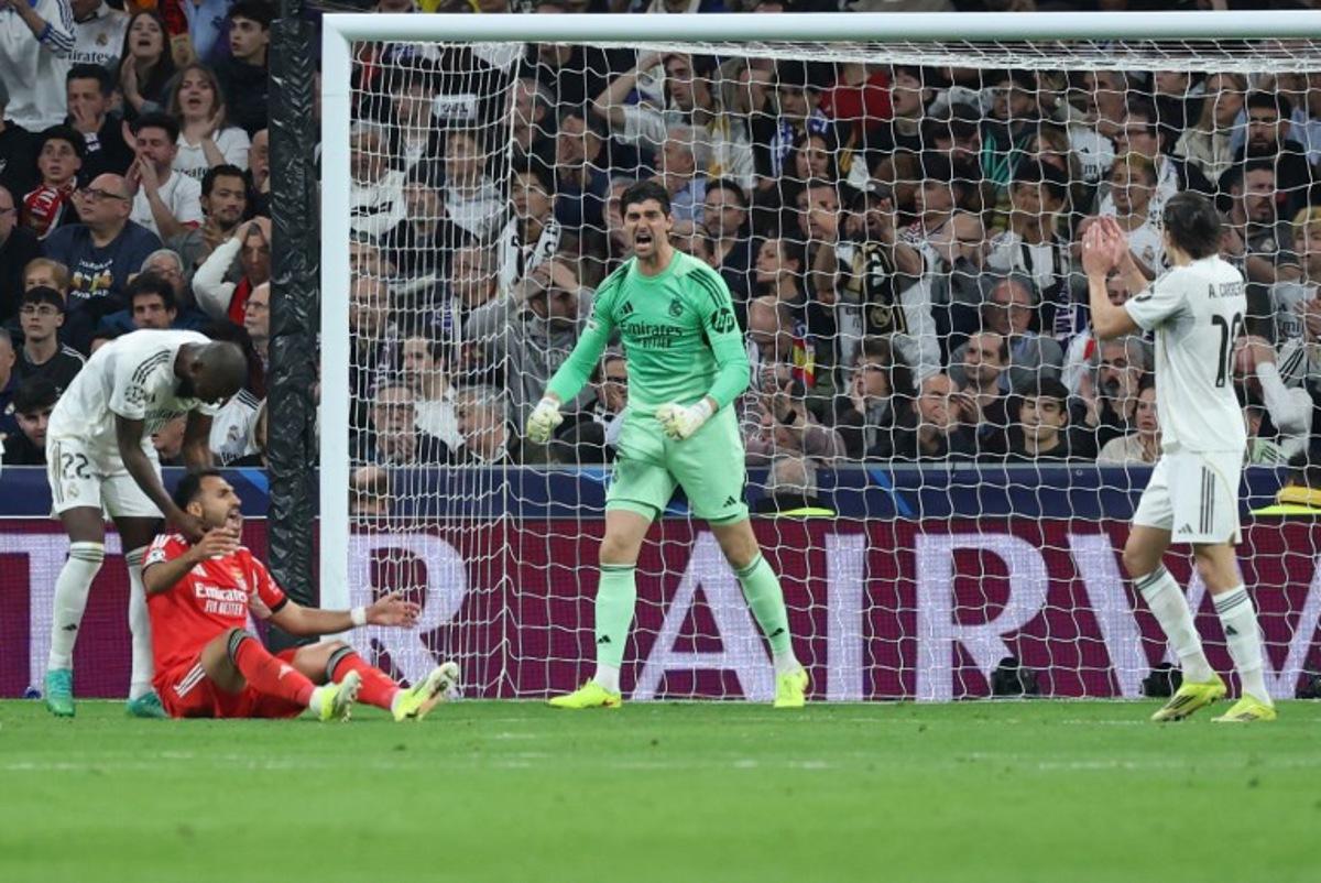 Real Madrid's Belgian goalkeeper #01 Thibaut Courtois reacts to saving the ball while Real Madrid's German defender #22 Antonio Ruediger talks with SL Benfica's Greek forward #14 Vangelis Pavlidis (L BOTTOM) during the UEFA Champions League knockout round play-off second leg football match between Real Madrid CF and SL Benfica at Santiago Bernabeu Stadium in Madrid on February 25, 2026.  Thomas COEX / AFP