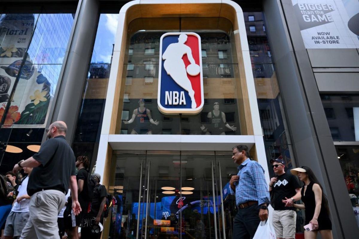 (FILES) People walk past an NBA fan store with the NBA logo in New York on July 8, 2024. The NBA is to review a proposal to create a new European basketball league which could feature up to 10 teams, a report said on March 25, 2025. Sports business news website Sportico said in a report that the European league proposal would be discussed at this week's NBA Board of Governors meeting. According to Sportico, league owners will consider a plan that includes eight to 10 franchises, including up to four teams who already play in the EuroLeague -- Europe's top club competition.  ANGELA WEISS / AFP