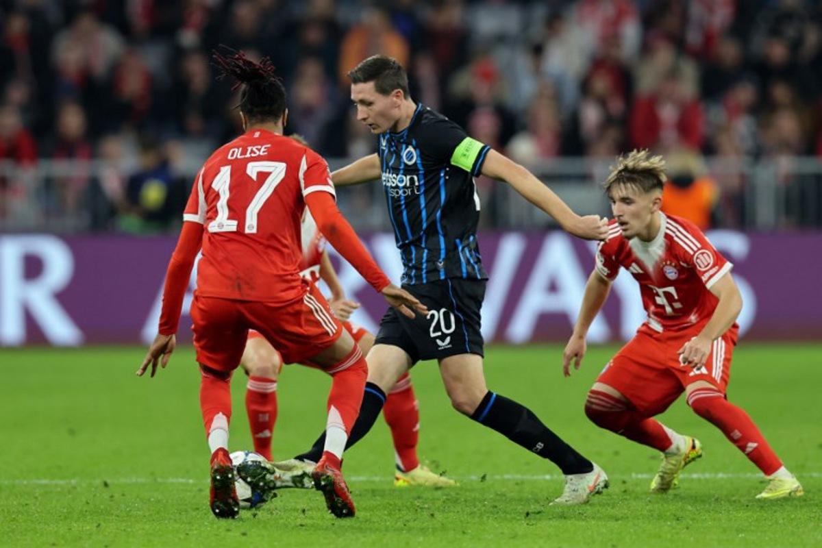 Club Brugge's Belgian midfielder #20 Hans Vanaken (C) vies for the ball with Bayern Munich's French midfielder #17 Michael Olise (L) and Bayern Munich's German midfielder #42 Lennart Karl during the UEFA Champions League football match between FC Bayern Munich and Club Brugge in Munich, southern Germany on October 22, 2025.  Alexandra BEIER / AFP