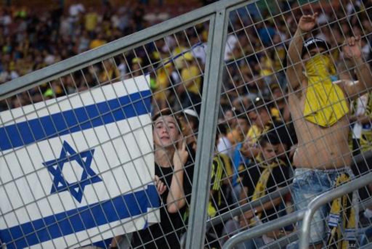 A supporter of Israeli football club Beitar Jerusalem holds an Israeli flags and gestures during their clubs return match against Belgium team Charleroi on July 23, 2015 at Teddy Stadium in Jerusalem. Beitar Jerusalem owner Eli Tabib announced after the first leg of Europa League match between Charleroi and Beitar was halted in Belgium that he was ashamed by the conduct of an extremist group of fans and intended to sell the team. AFP PHOTO / MENAHEM KAHANA