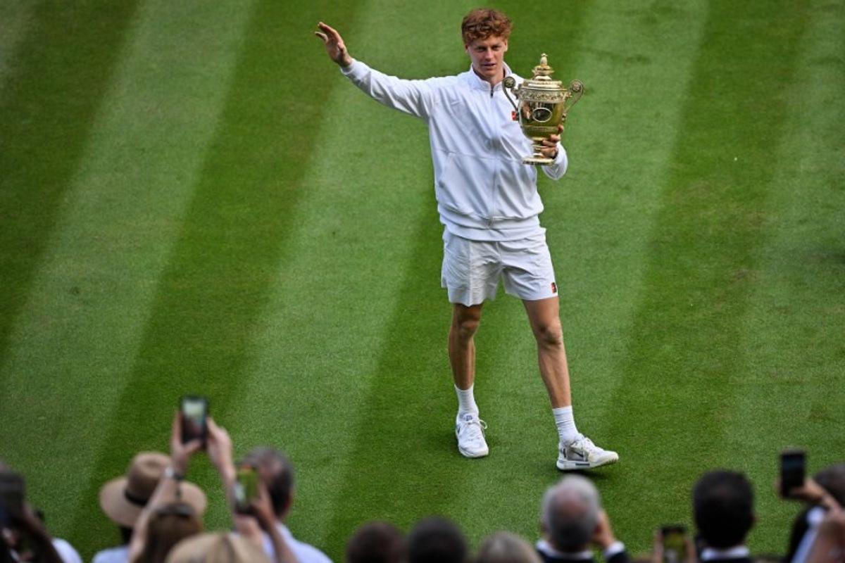 Italy's Jannik Sinner greets supporters as he celebrates with the winner's trophy following his victory against Spain's Carlos Alcaraz at the end of their men's singles final tennis match on the fourteenth day of the 2025 Wimbledon Championships at The All England Lawn Tennis and Croquet Club in Wimbledon, southwest London, on July 13, 2025.  Glyn KIRK / AFP