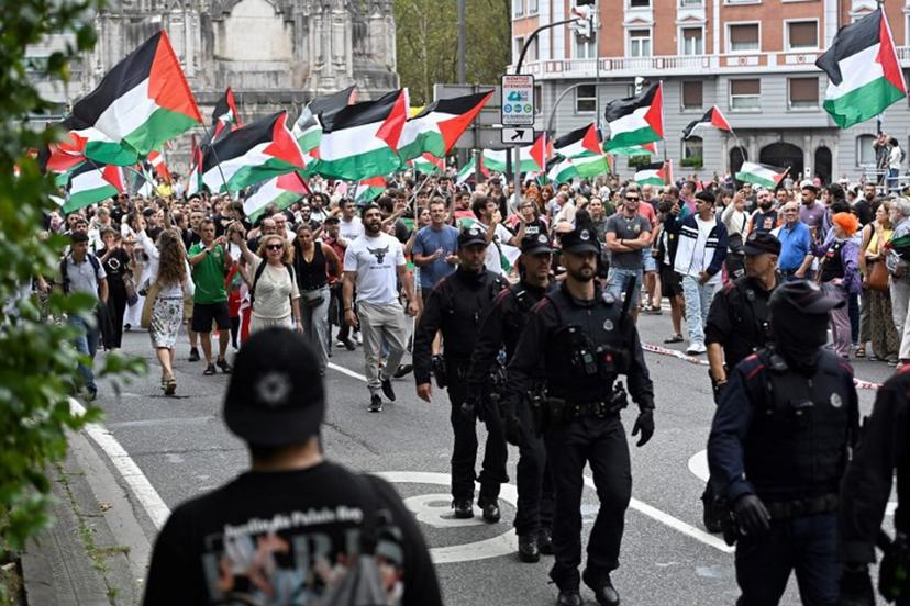 Pro-Palestinian protesters holding Palestinian flags walk behind Basque regional police 'Ertzaintza' officers as they demonstrate following the Vuelta 11th stage, in Bilbao, on September 3, 2025. Pro-Palestinian protest forces Vuelta stage to be shortened and to take the time at 3 kilometres before the line, according to the organisers, AFP reports. ANDER GILLENEA / AFP