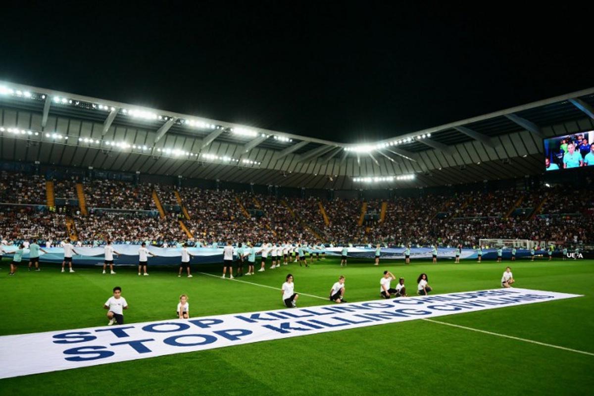 Mascots hold a banner which reads "Stop killing children, Stop killing civilians" on the pitch ahead of the 2025 UEFA Super Cup final football match between Paris Saint-Germain (FRA) and Tottenham Hotspur FC (ENG) at the Friuli stadium, in Udine, on August 13, 2025.  Marco BERTORELLO / AFP