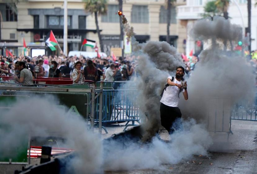 A man throws a smoke flare back at police after Pro-Palestinians protestors invaded the street  forcing race organisers to abandon the 21st and final stage of the Vuelta a Espana 2025, in Madrid on September 14, 2025.    Thomas COEX / AFP