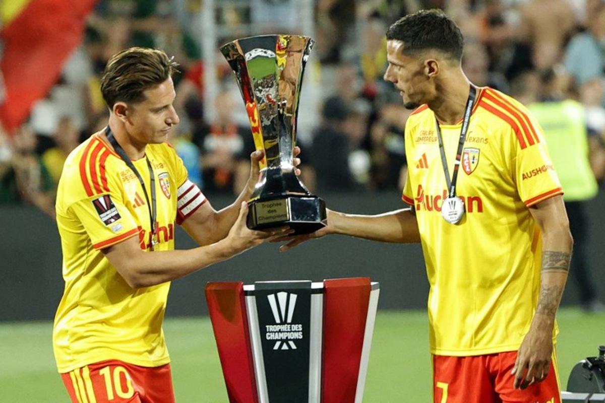 Lens' French forward #10 Florian Thauvin (L) and Lens' French forward #07 Florian Sotoca take the championship trophy to celebrate with teammates after winning the French Super Cup (Trophee des Champions) football match between RC Lens and Paris Saint-Germain (PSG) at the Stade Bollaert-Delelis in Lens, northern France on August 16, 2026. GEOFFROY VAN DER HASSELT / AFP