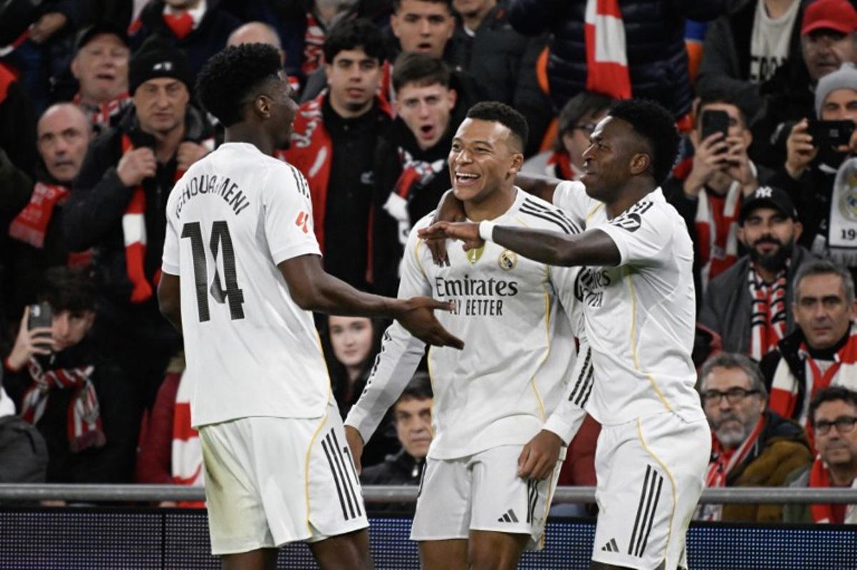 Real Madrid's French forward #10 Kylian Mbappe (C) celebrates with teammates Real Madrid's Brazilian forward #07 Vinicius Junior (R) and Real Madrid's French midfielder #14 Aurelien Tchouameni after scoring his team's third goal during the Spanish league football match between Athletic Club Bilbao and Real Madrid CF at the San Mames stadium in Bilbao on December 3, 2025. ANDER GILLENEA / AFP