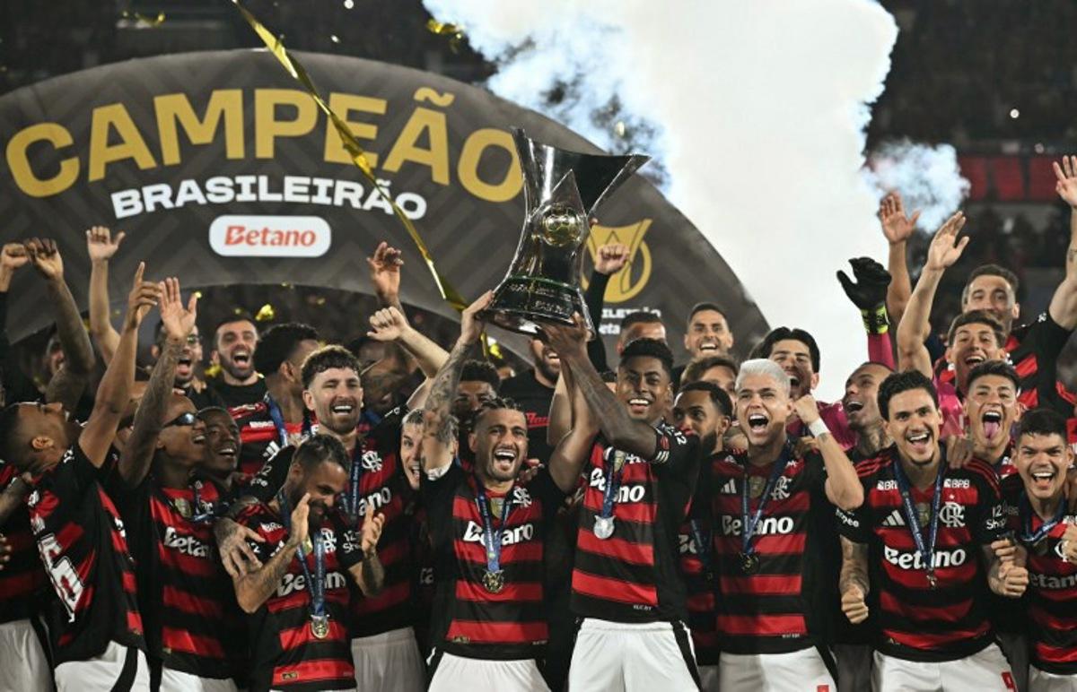 Flamengo's Uruguayan midfielder #10 Giorgian de Arrascaeta (C-L) and forward #27 Bruno Henrique (C-R) lift the Brasileirao trophy after winning the Brasileirao Serie A football match between Flamengo and Ceara at Maracana Stadium in Rio de Janeiro, Brazil, on December 3, 2025. Mauro PIMENTEL / AFP
