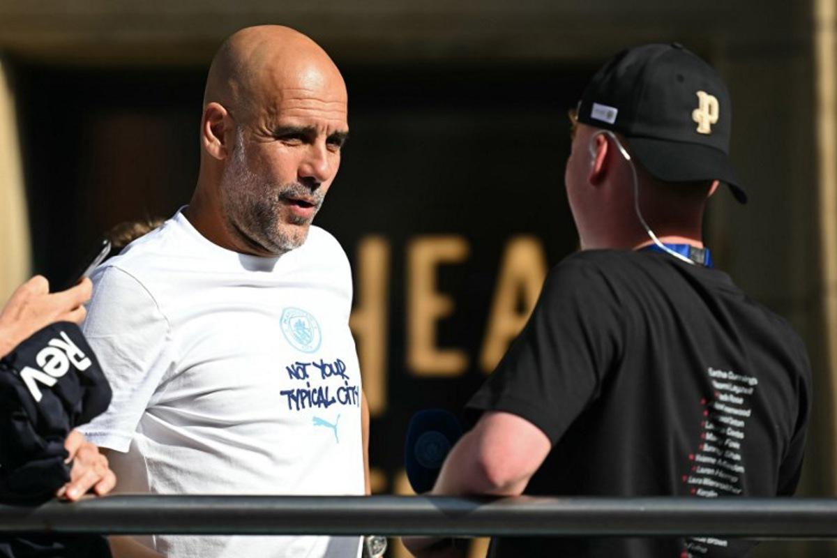 Departing Manchester City manager Pep Guardiola hops onto the bus with his youth players at the start of the winner's parade by the Manchester City team after their victories in the two domestic cup competitions on May 25, 2026, in central Manchester, north-west England. Paul ELLIS / AFP
