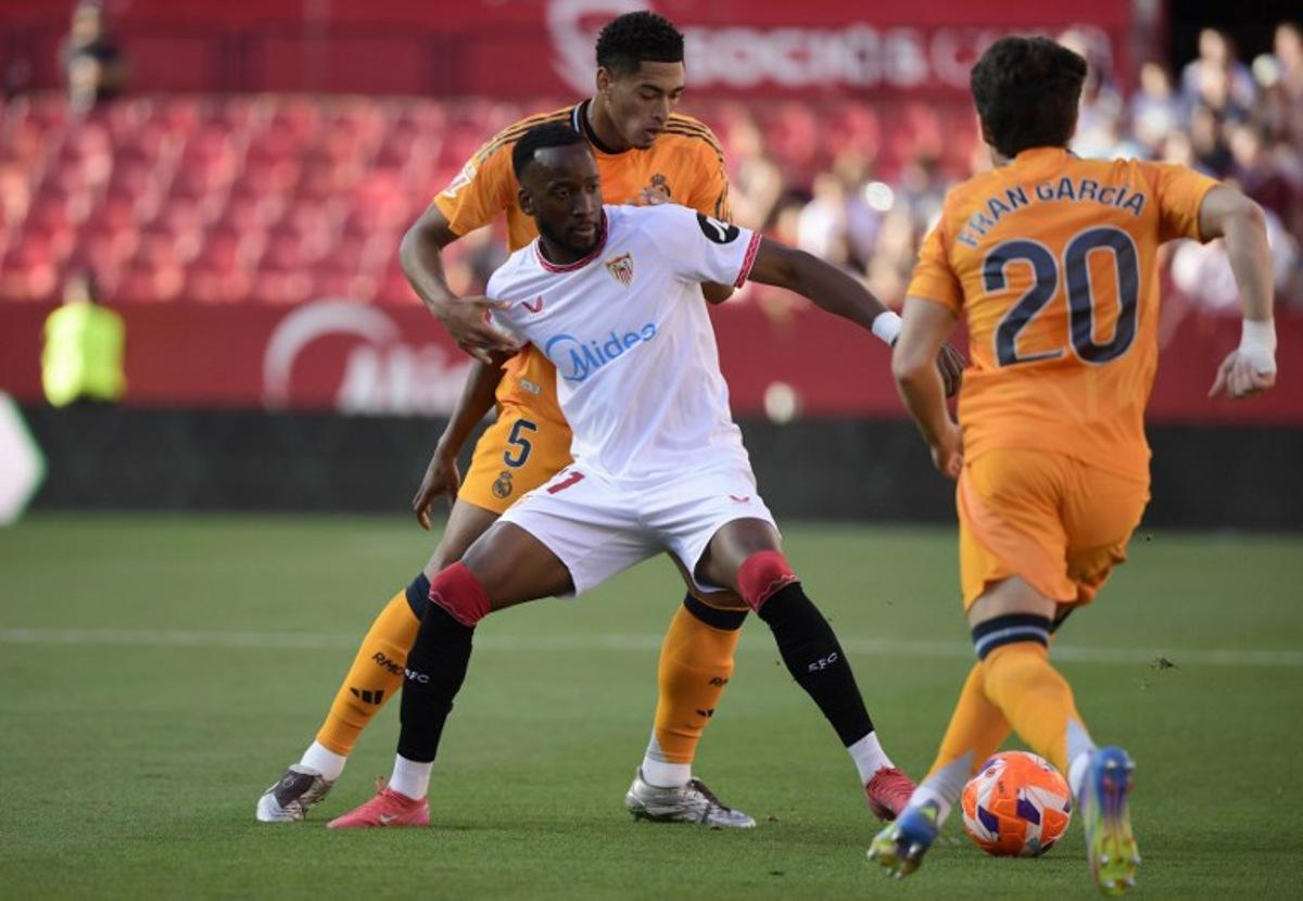Sevilla's Belgian forward #11 Dodi Lukebakio (C) fights for the ball with Real Madrid's English midfielder #05 Jude Bellingham during the Spanish league football match between Sevilla FC and Real Madrid CF at Ramon Sanchez Pizjuan Stadium in Seville on May 18, 2025. CRISTINA QUICLER / AFP