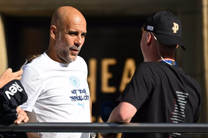 Departing Manchester City manager Pep Guardiola hops onto the bus with his youth players at the start of the winner's parade by the Manchester City team after their victories in the two domestic cup competitions on May 25, 2026, in central Manchester, north-west England. Paul ELLIS / AFP