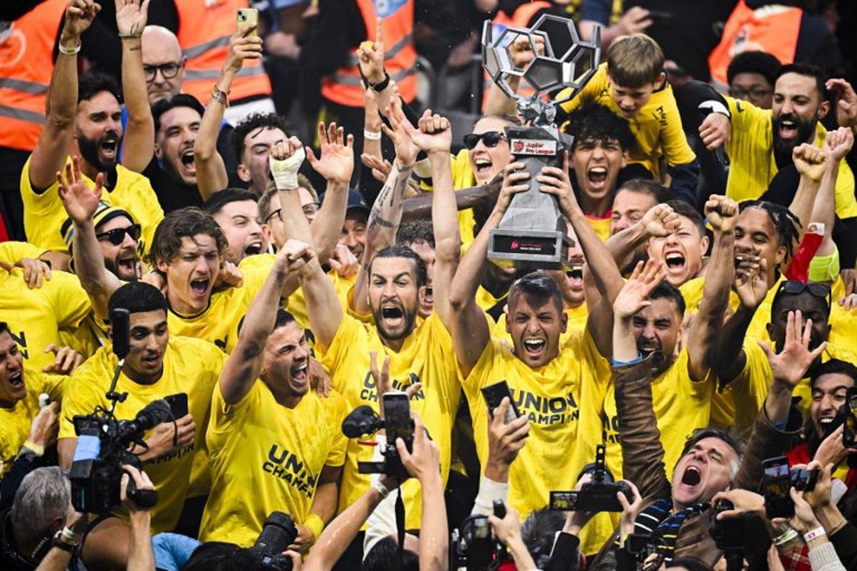 Union's Luxembourgish goalkeeper #49 Anthony Moris (3rd R) raises the trophy as he celebrates with teammates and supporters their Belgian championship title after winning the Belgian Pro League champions' play-off football match (day 10 of 10) between Royale Union Saint-Gilloise and KAA Gent, at the Joseph Marien Stadium in Brussels, on May 25, 2025. LAURIE DIEFFEMBACQ / AFP