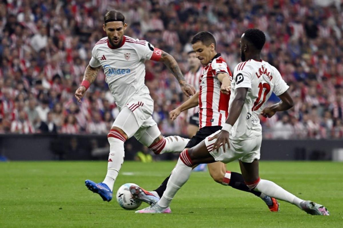 Sevilla's Serbian midfielder #06 Nemanja Gudelj (L), Athletic Bilbao's Spanish midfielder #16 Inigo Ruiz de Galarreta and Sevilla's Belgian forward #10 Dodi Lukebakio fight for the ball during the Spanish league football match between Athletic Club Bilbao and Sevilla FC at San Mames Stadium in Bilbao on August 17, 2025. ANDER GILLENEA / AFP