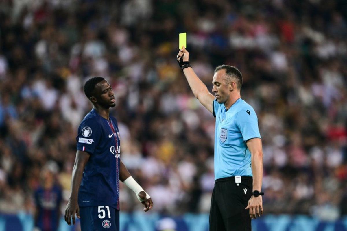 Portuguese referee Joao Pinheiro (R) shows Paris Saint-Germain's Ecuadoran defender #51 Willian Pacho (L) a yellow card as he books him for a foul during the 2025 UEFA Super Cup final football match between Paris Saint-Germain (FRA) and Tottenham Hotspur FC (ENG) at the Friuli stadium, in Udine, on August 13, 2025. Marco BERTORELLO / AFP