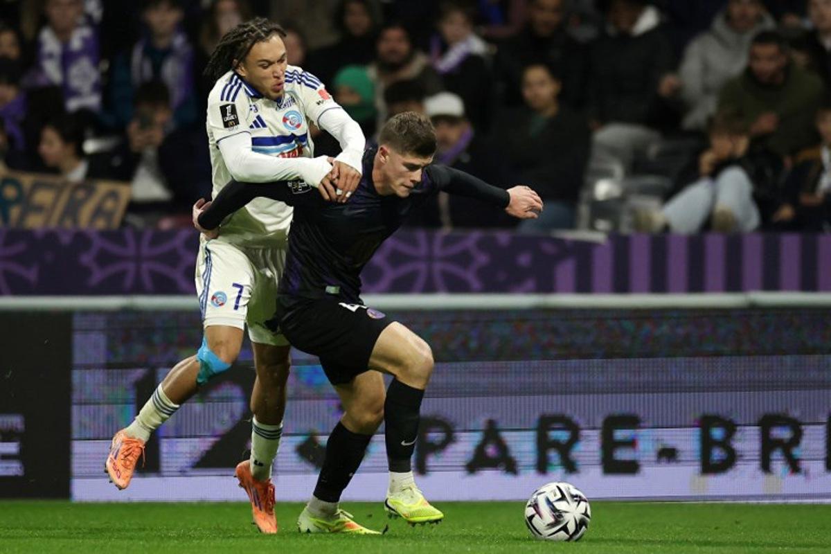 Strasbourg's Belgian midfielder #07 Diego Moreira (L) fights for the ball with Toulouse's English defender #04 Charlie Cresswell (R) during the French L1 football match between Toulouse FC and RC Strasbourg Alsace at the TFC Stadium in Toulouse, southwestern France, on December 6, 2025. Valentine CHAPUIS / AFP