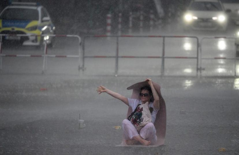 A woman uses a yoga mat to take shelter from the pouring rain as she takes part in the international yoga day, on June 21, 2026 in Berlin, Germany. RALF HIRSCHBERGER / AFP