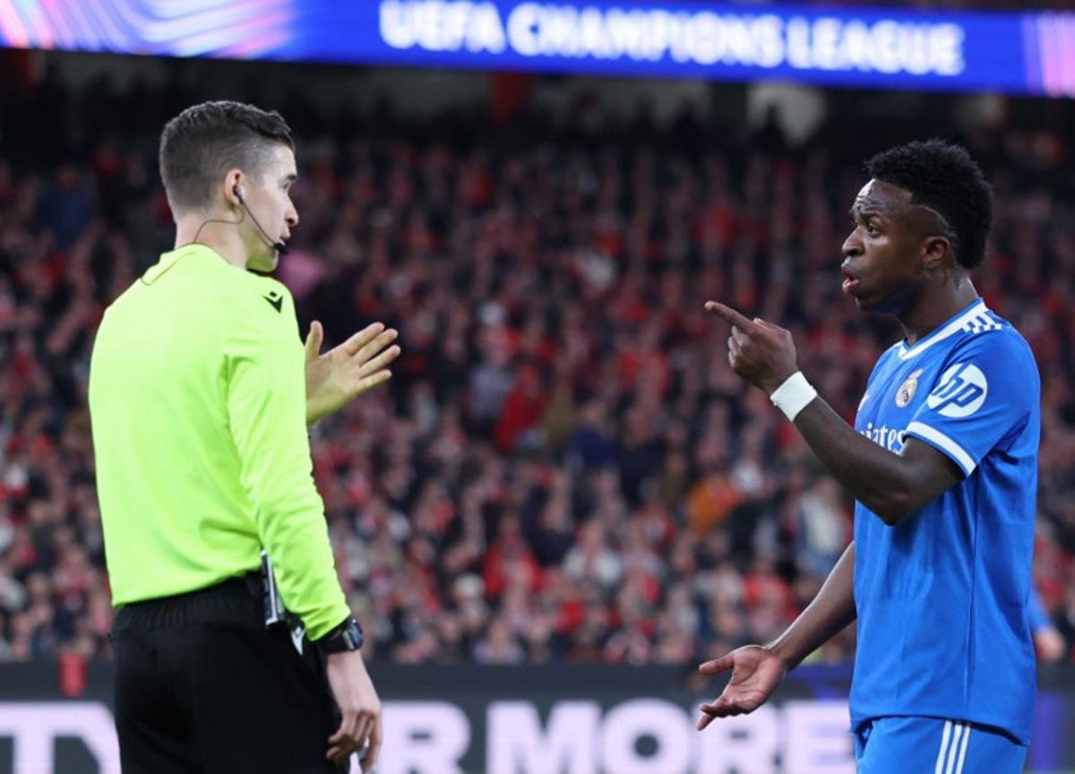 Real Madrid's Brazilian forward #07 Vinicius Junior talks with French referee Francois Letexier during the UEFA Champions League knockout round play-off first leg football match between SL Benfica and Real Madrid CF at Estadio da Luz in Lisbon on February 17, 2026. PATRICIA DE MELO MOREIRA / AFP