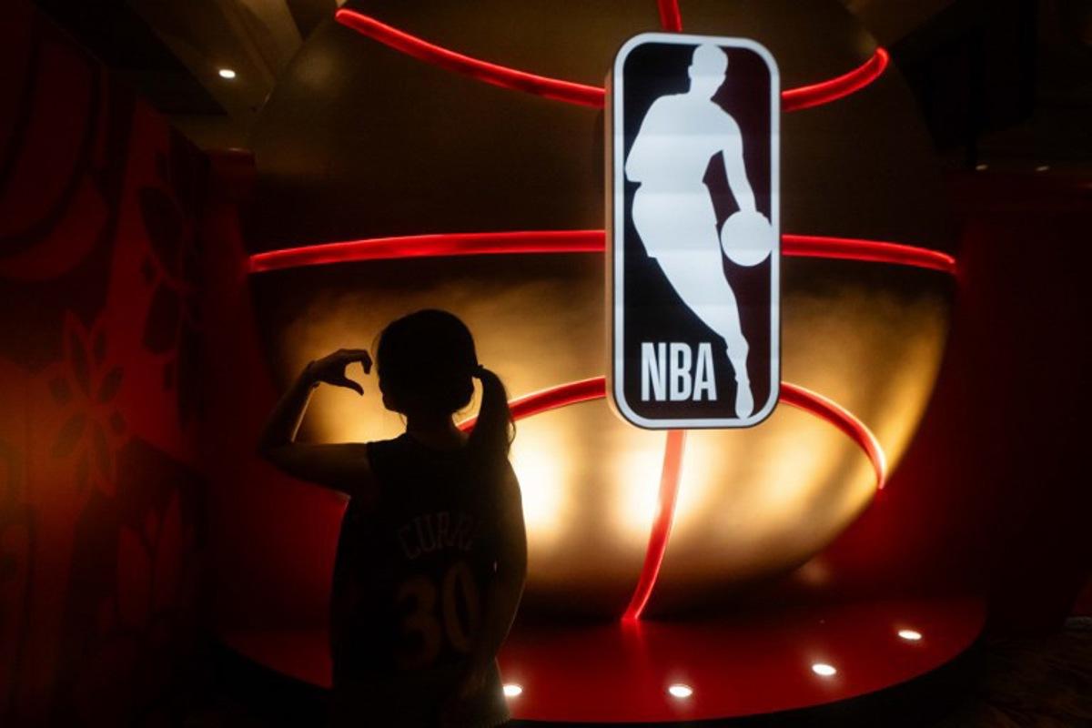 A fan poses next to the National Basketball Association logo before the NBA pre-season basketball game between the Phoenix Suns and Brooklyn Nets at the Venetian Arena in Macau on October 12, 2025. Eduardo Leal / AFP